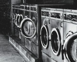 A row of industrial washing machines in an urban laundromat, showcasing steel finish.